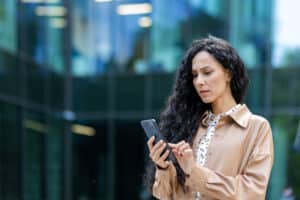 Unternehmerin blickt besorgt auf ihr Smartphone vor einem Bürogebäude